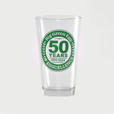 A clear drinking glass with a green circular 'Big Green Egg' logo featuring '50 YEARS OF EGGCELLENCE' and '1974-2024' printed on the front, set against a light gray background.