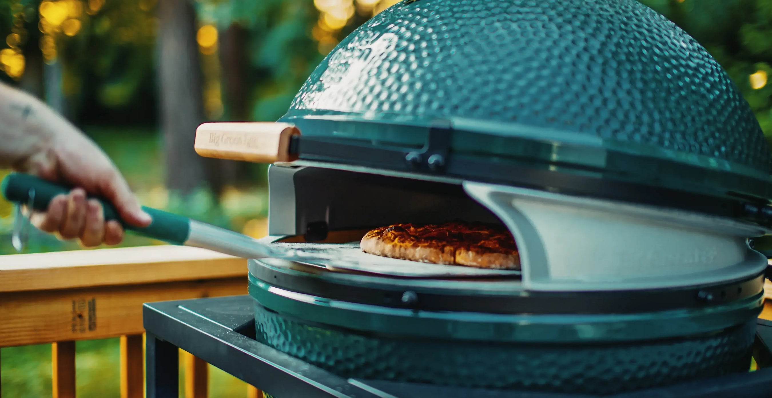 Person using a grill to cook a pizza on a wooden deck