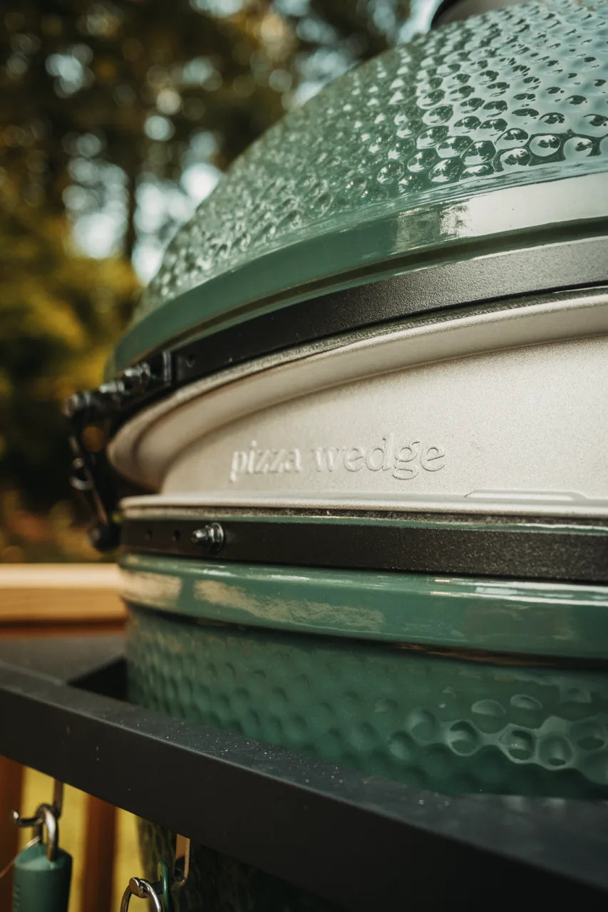 Close-up of a big green egg modified to be a pizza oven with 'pizza wedge' branding outdoors.