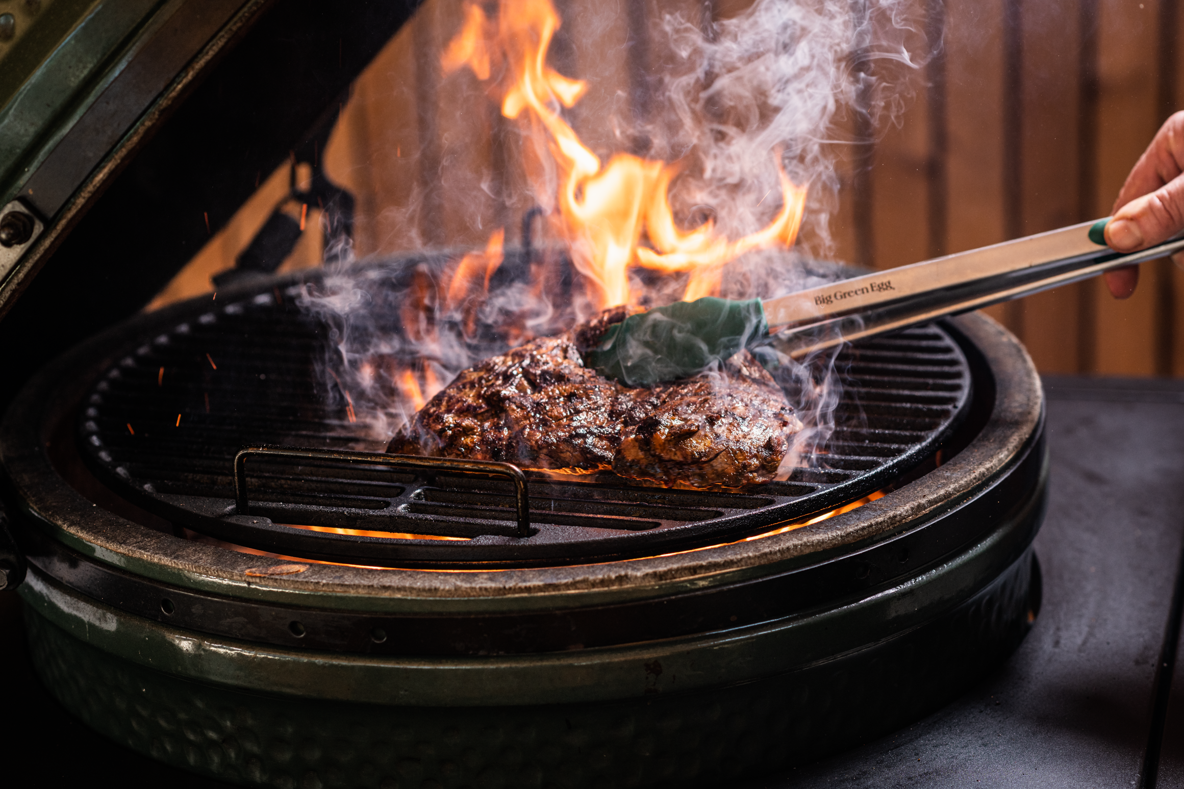 Hamburger patty being cooked on a grill with flames and smoke.