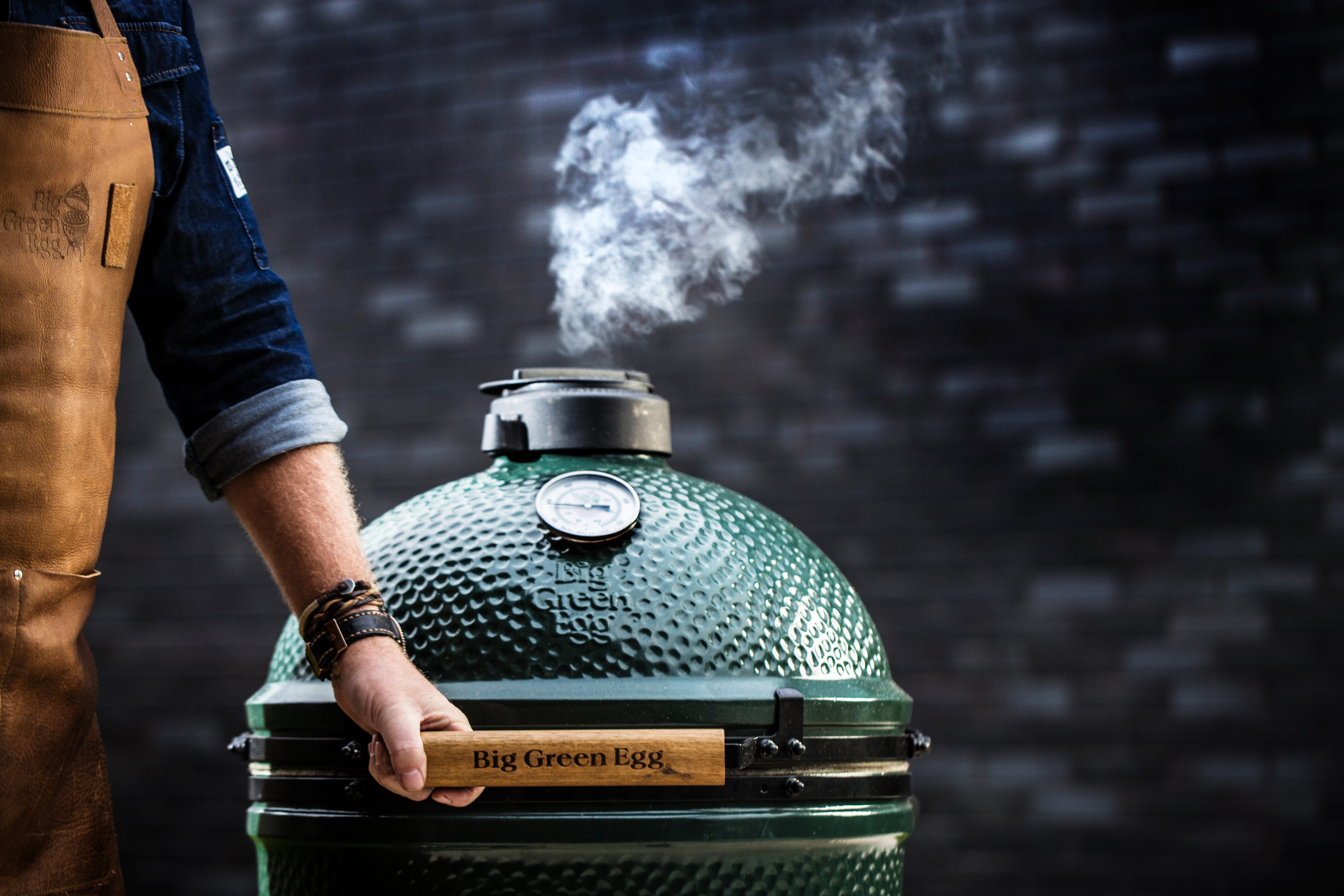 hand opening large biggreenegg with smoke