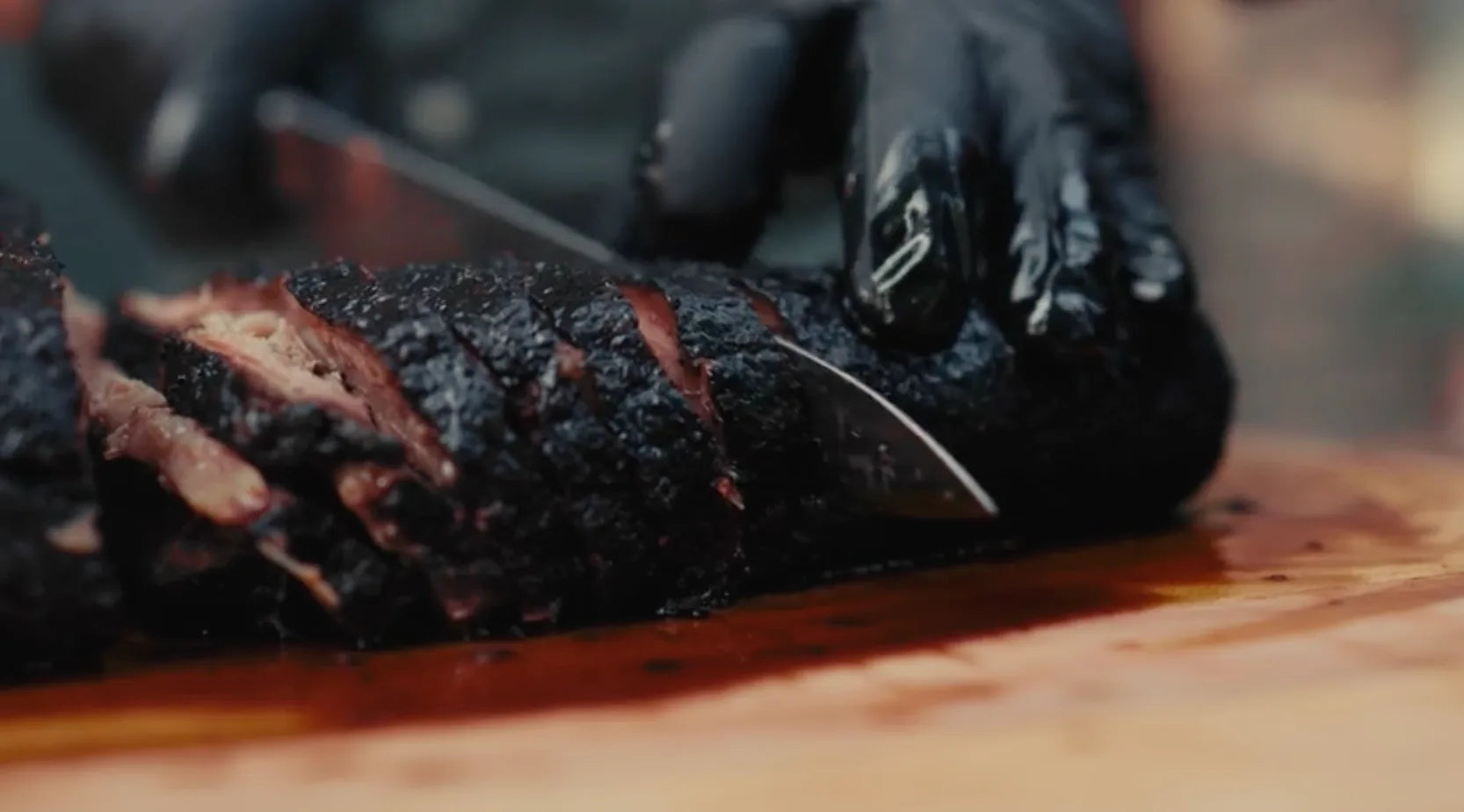 Sliced smoked brisket on cutting board with Big Green Egg smoker in background.