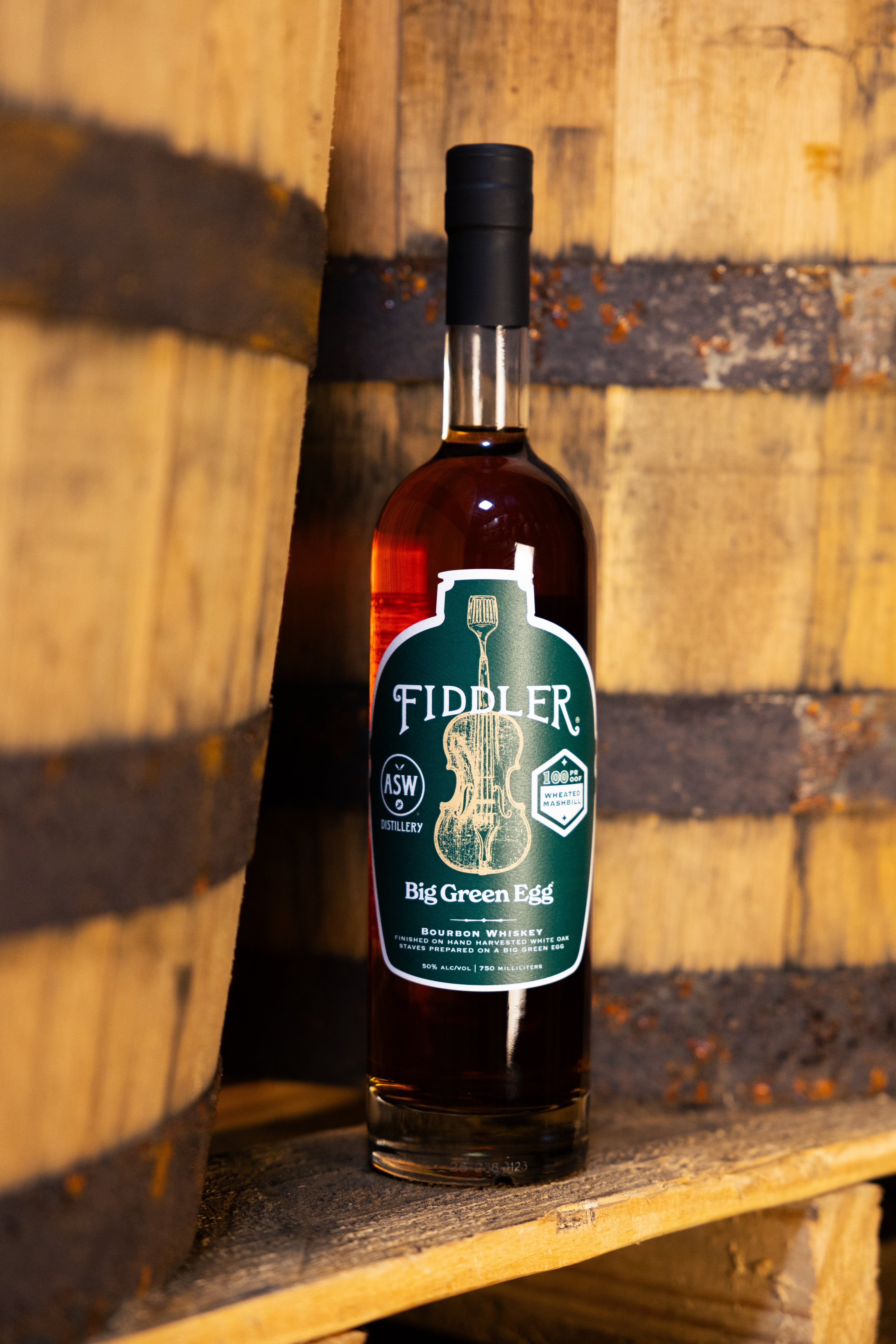 Bottle of Fiddler's Big Green Flag whiskey against a wooden barrel background