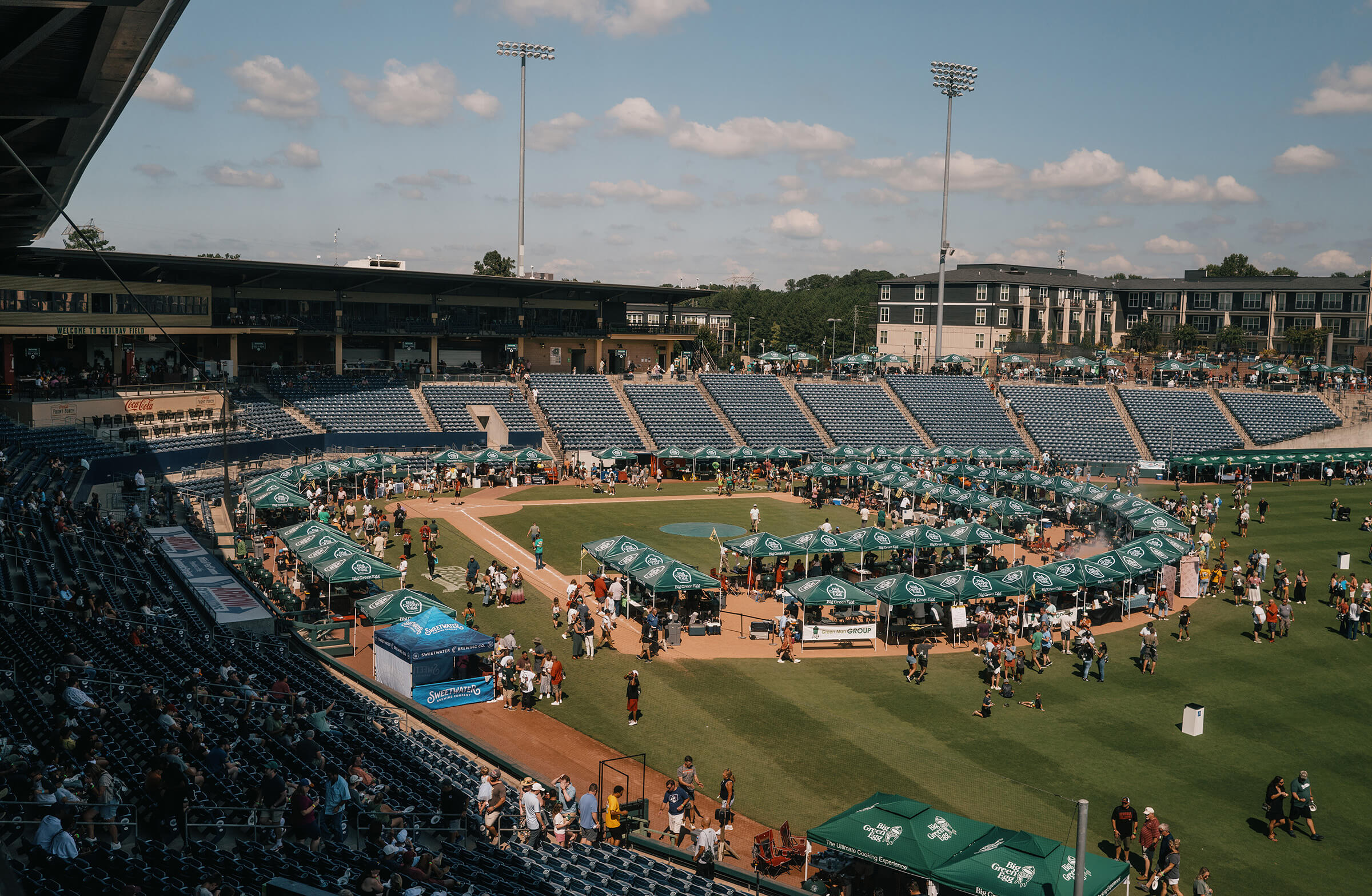 Outdoor event with green tents and people in a stadium setting