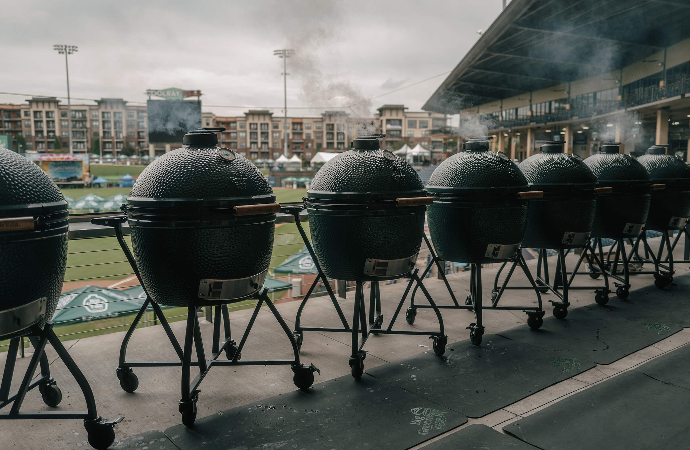 Row of large barbecue grills on wheels at a sports stadium.