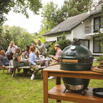 Group of people enjoying a barbecue outdoors with a large green ceramic kamado grill.