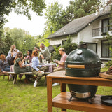 Group of people enjoying a barbecue outdoors with a large green ceramic kamado grill.