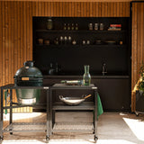 Outdoor kitchen setup with a Big Green Egg grill and shelves in a wooden cabin.