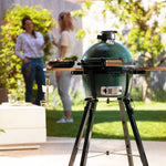 Green egg ceramic kamado grill on a stand with people in the background in a garden setting