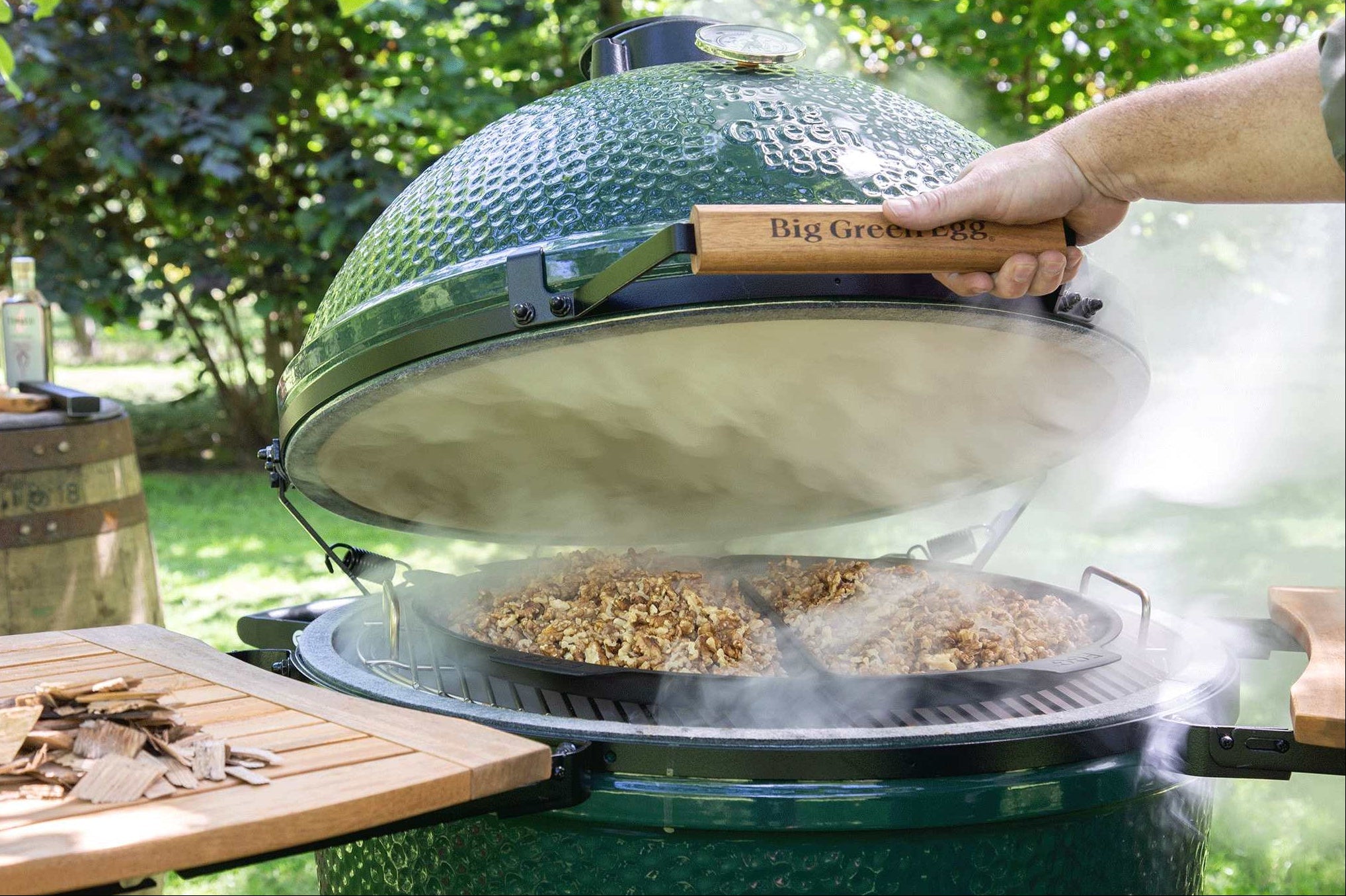Person using a Big Green Egg grill outdoors with food cooking inside