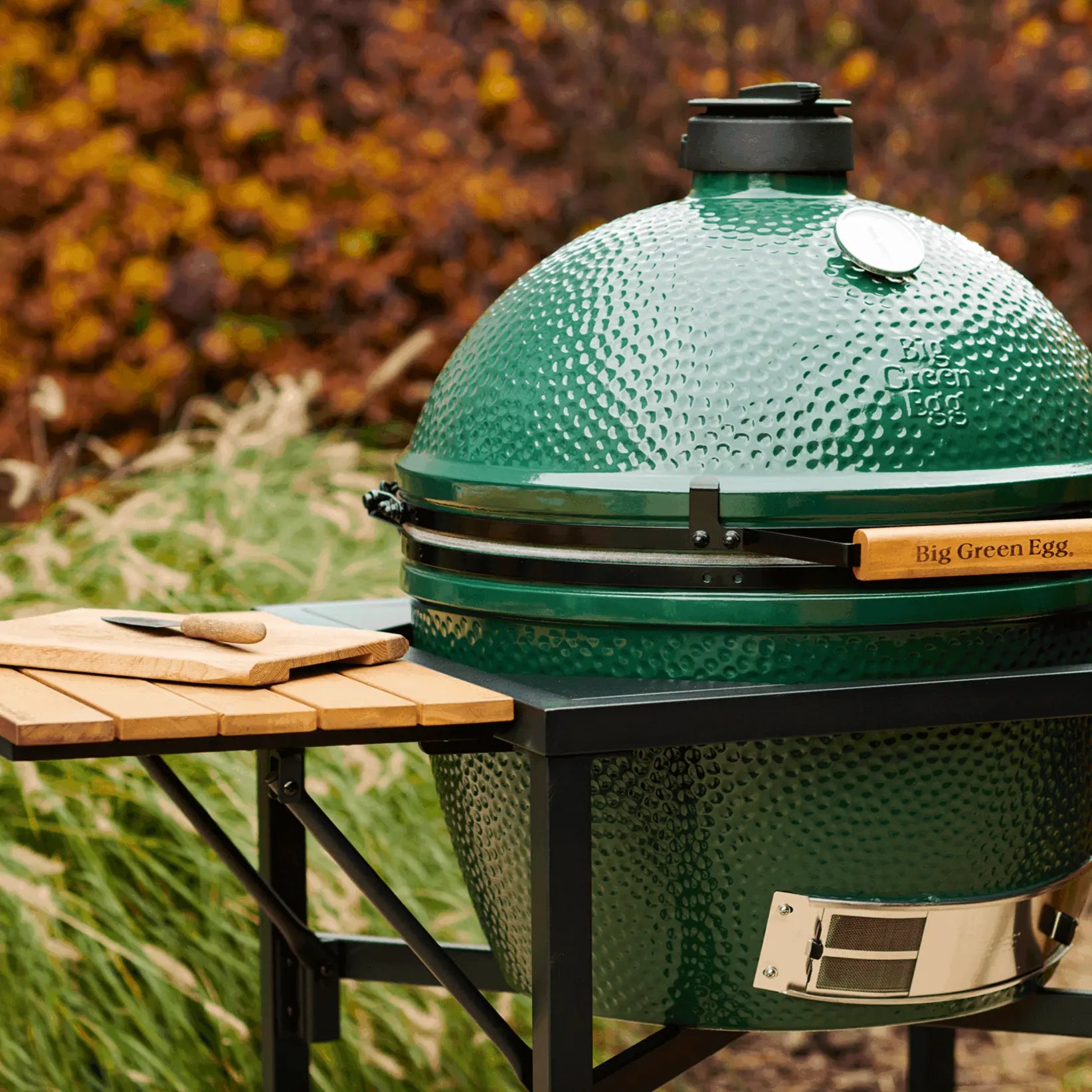 Green Big Green Egg ceramic kamado grill on a wooden table outdoors with a blurred natural background