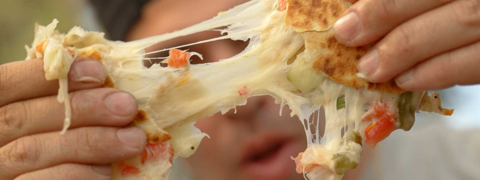 Man pulling a cheesy quesadilla apart in front of his face