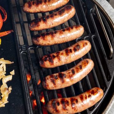 Brats, Peppers and Onions grill on cast iron grid in a Big Green Egg